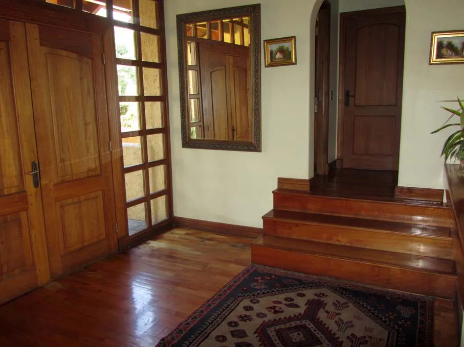 Interior shot of a home's entryway with wood floors, doors, and stairs. A patterned rug sits at the base of the stairs. A mirror hangs on the wall.