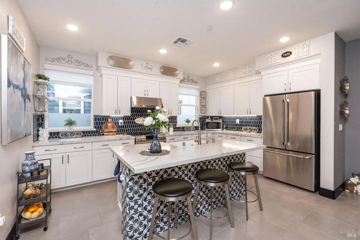 Bright kitchen with white cabinets, stainless steel appliances, and a patterned island with three stools.