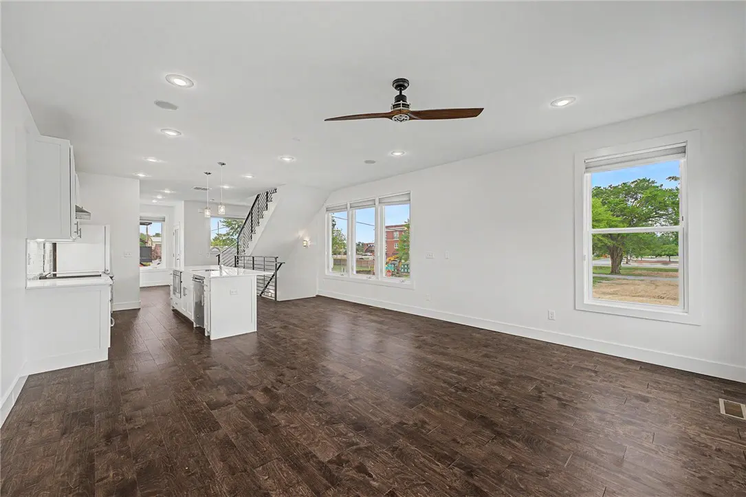 Bright, open-concept living space with dark wood floors, white walls, and a modern kitchen. Large windows offer natural light and views of the outdoors.