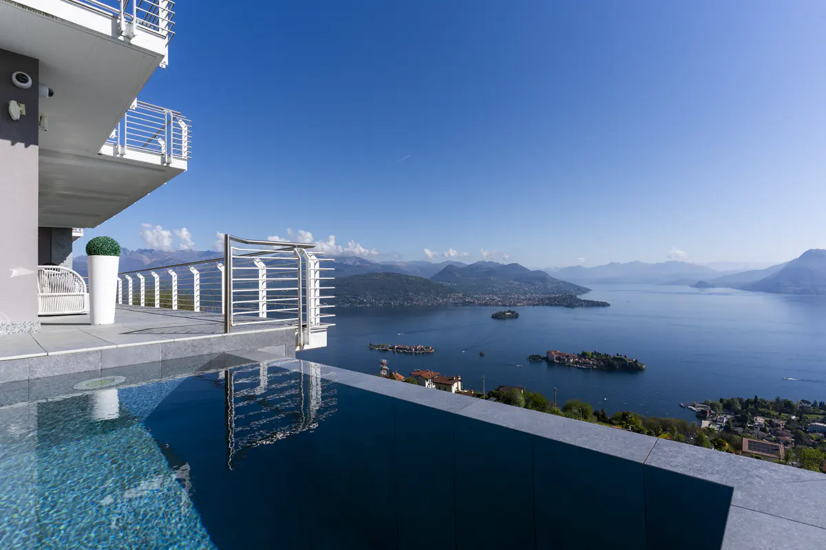 Infinity pool overlooking Lake Maggiore, Italy. Mountains and islands are visible in the distance under a clear blue sky.