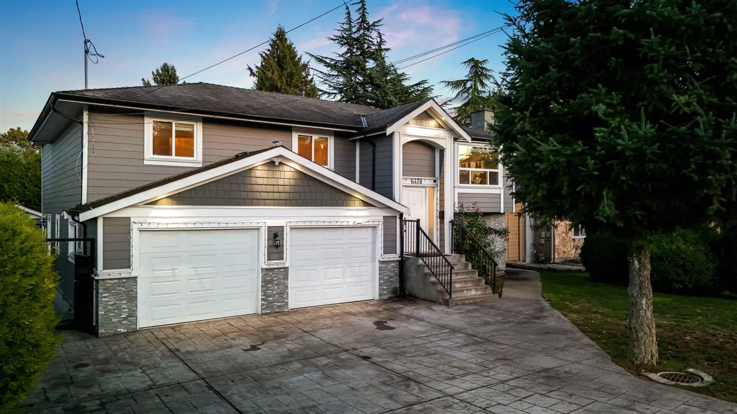Two-story gray house with a two-car garage, white doors, and a concrete driveway. Trees surround the property.