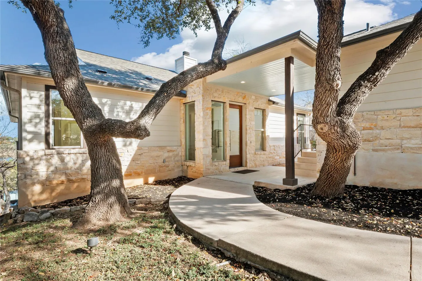 Exterior view of a modern home with a stone and white siding facade, a curved walkway, and mature trees.