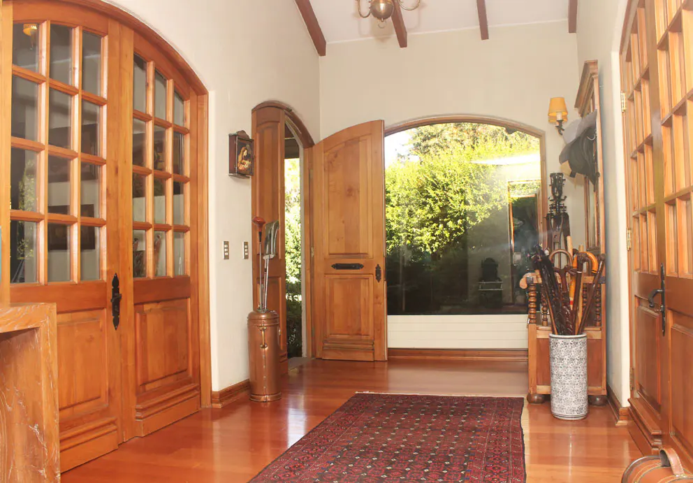 A foyer with wood floors, doors, and trim. A rug is on the floor. A garden is visible through an arched doorway.