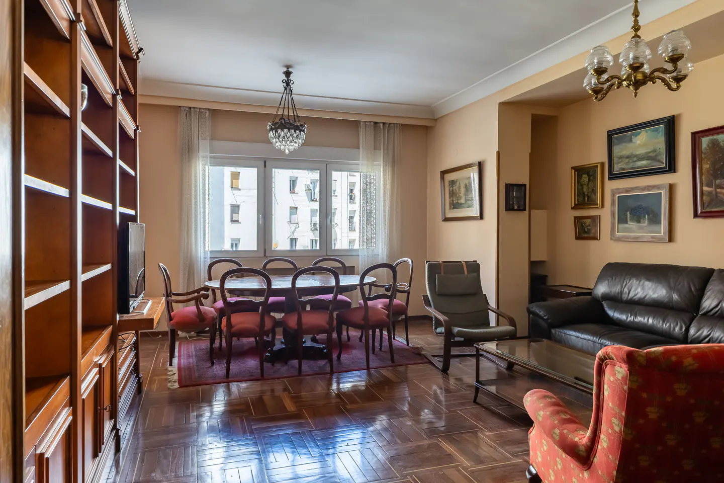 A living and dining room with a dark wood floor, a dining table with red chairs, and a brown leather sofa.