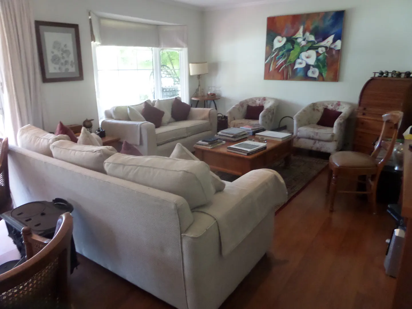 Living room with white sofas, floral armchairs, and a wooden coffee table with books. A painting of white flowers hangs above.