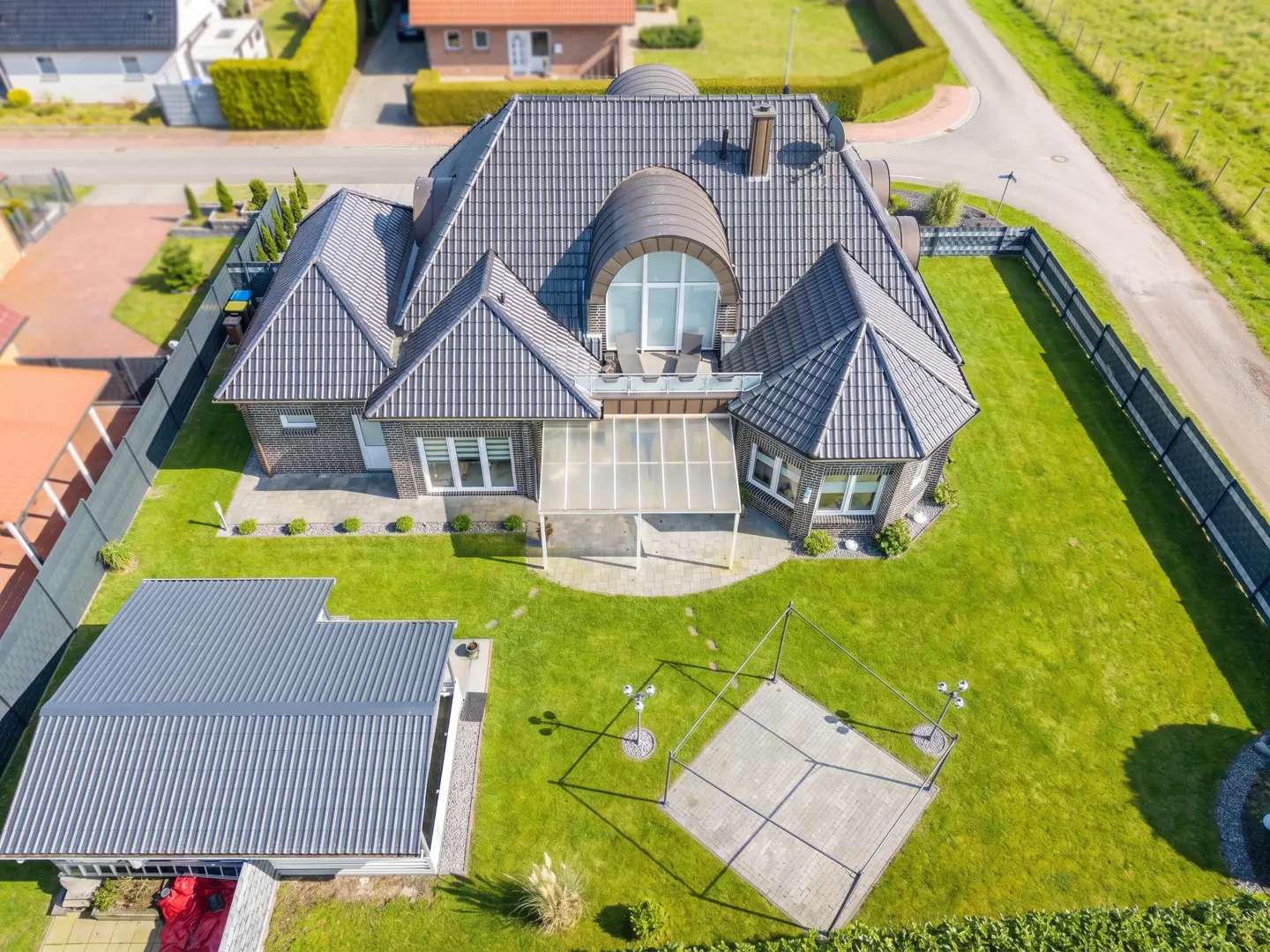 Aerial view of a modern brick house with a gray roof, green lawn, patio, and detached garage.