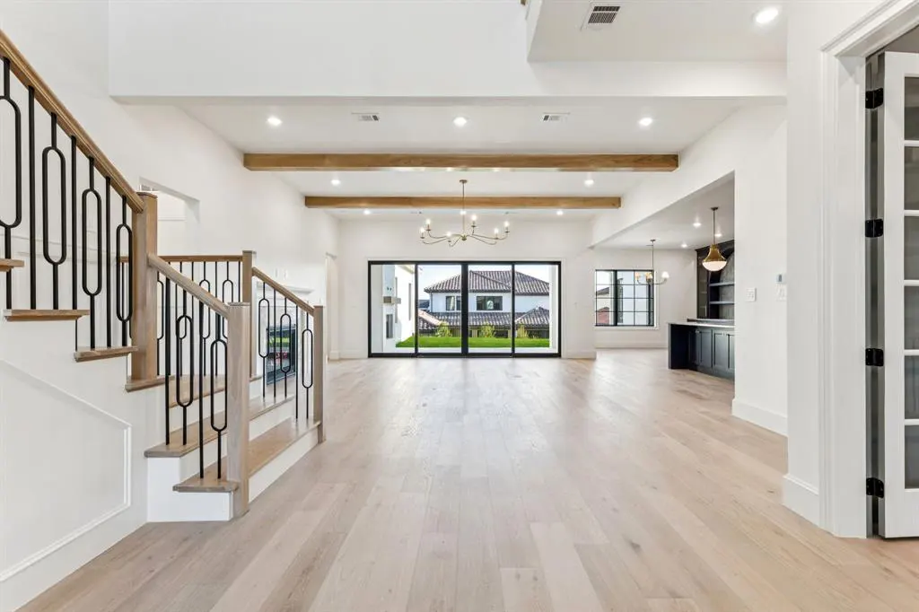 Bright, open-concept living room with light wood floors, white walls, and black-framed windows. A staircase with black metal railings is on the left.