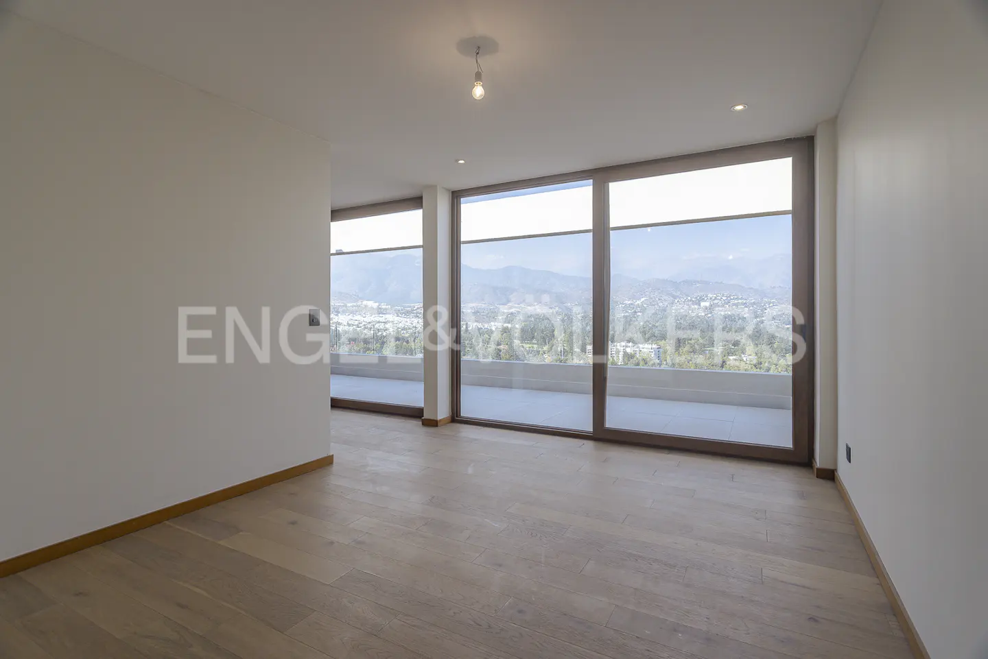 Bright, empty room with light wood floors and white walls. Large windows offer a view of mountains and a city.