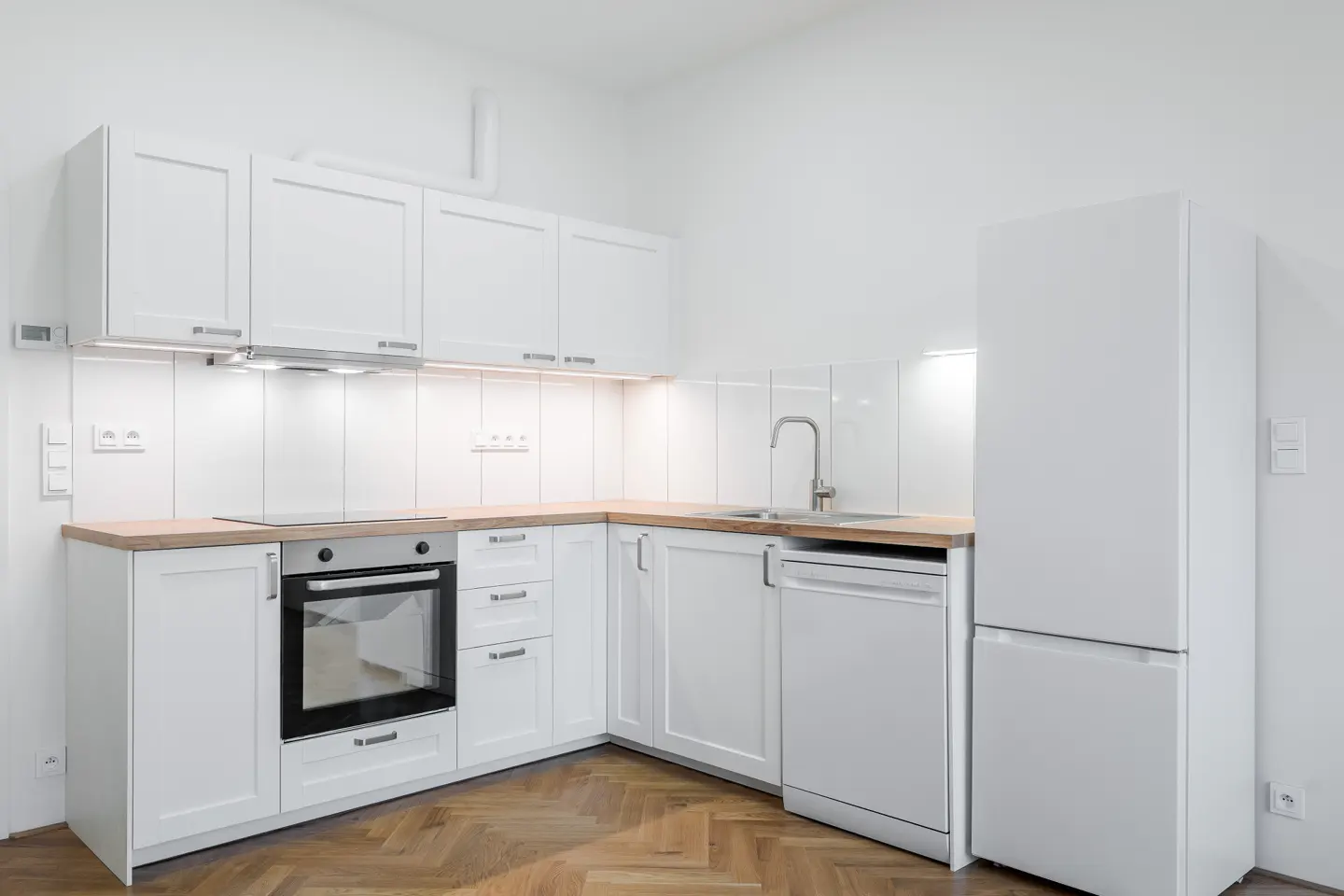 Bright, modern kitchen with white cabinets, wood countertops, stainless steel appliances, and herringbone wood floors.