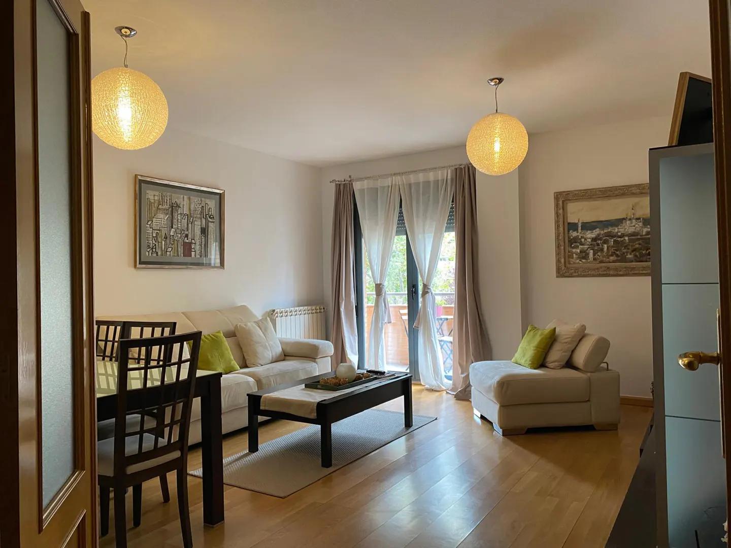 Bright living room with cream sofa, armchair, dark wood coffee table, dining set, and balcony doors with sheer curtains.