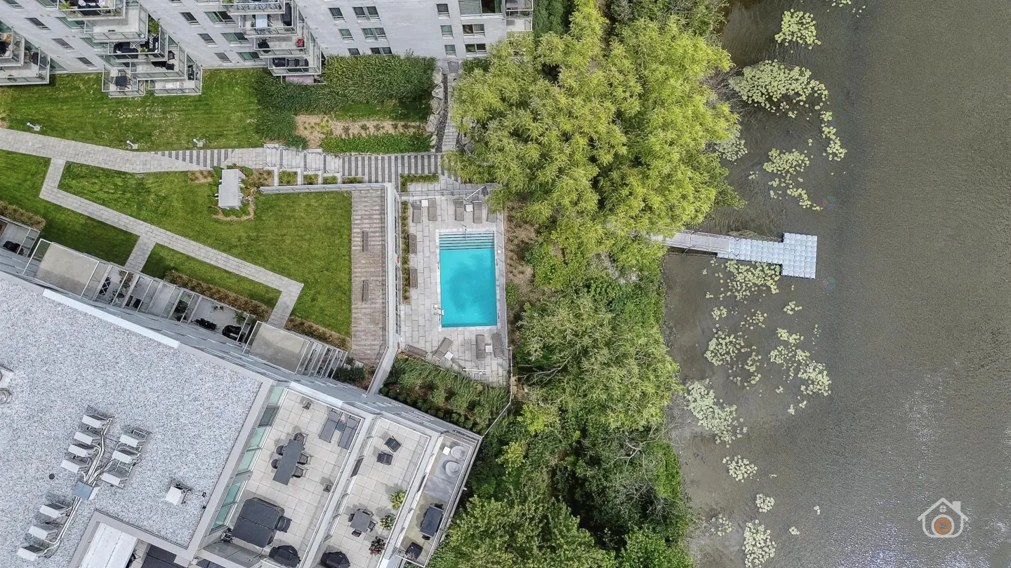 Aerial view of a modern apartment complex with a pool, green lawn, and a dock on the water.