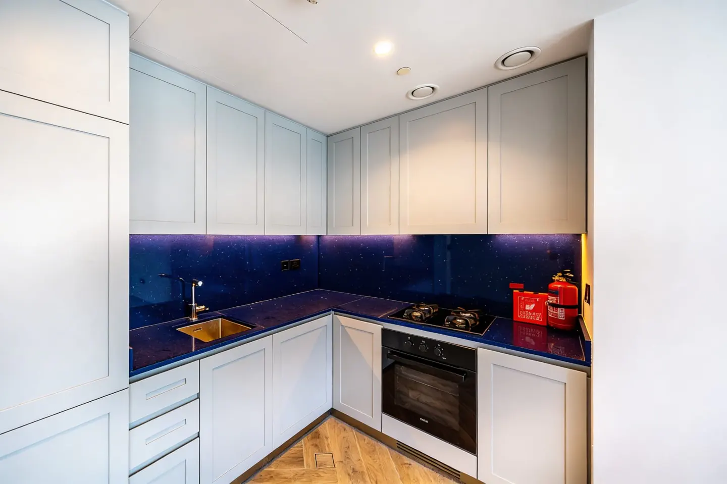 A modern kitchen with light blue cabinets, a dark blue countertop, and stainless steel appliances.
