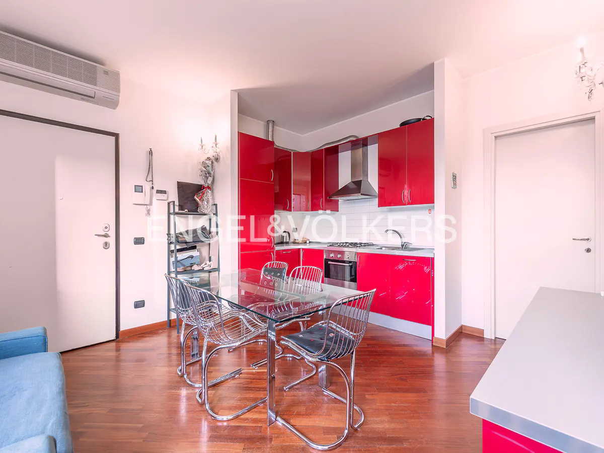A modern kitchen with red cabinets, stainless steel appliances, and a glass table with chrome chairs on a wood floor.