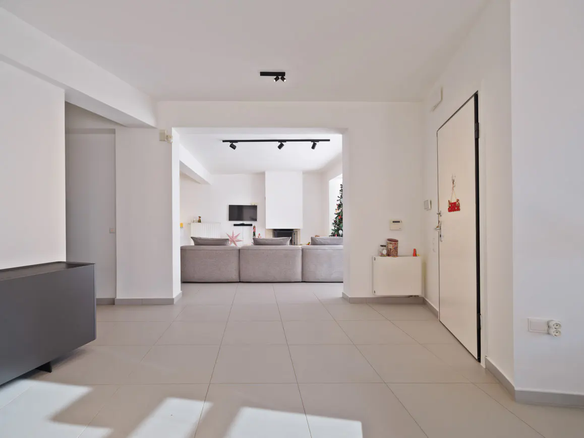 Bright, open-plan living room with white walls, light tile floors, a large grey sectional sofa, and track lighting.