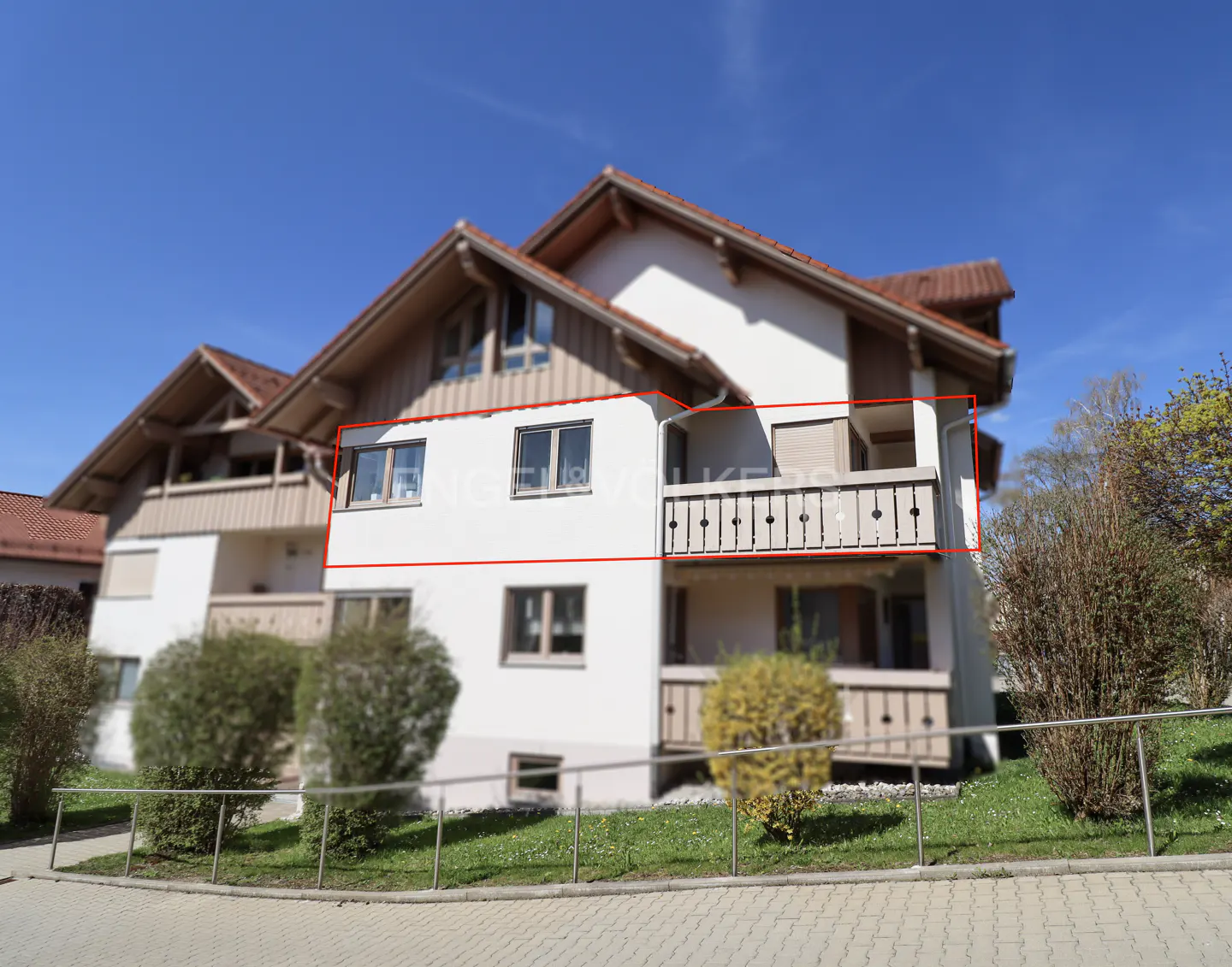 Exterior view of a white two-story building with a balcony and brown roof against a blue sky.