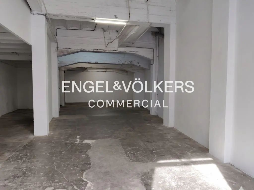 Empty commercial space with concrete floors and white walls, columns, and ceiling. The Engel & Völkers Commercial logo is superimposed.
