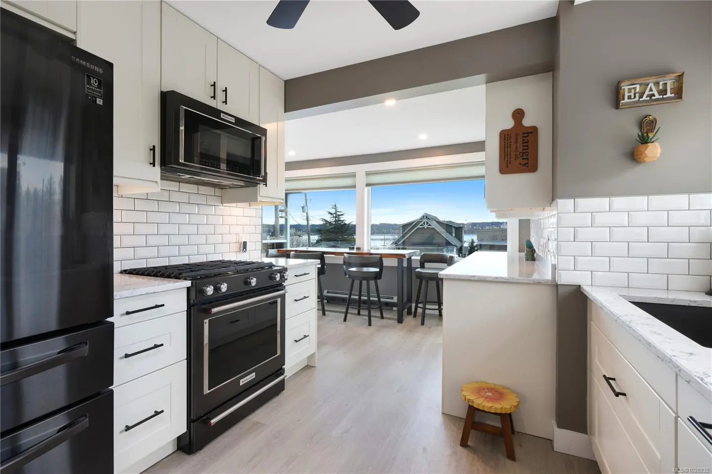 A bright kitchen with white cabinets, black appliances, and a large window overlooking a lake.