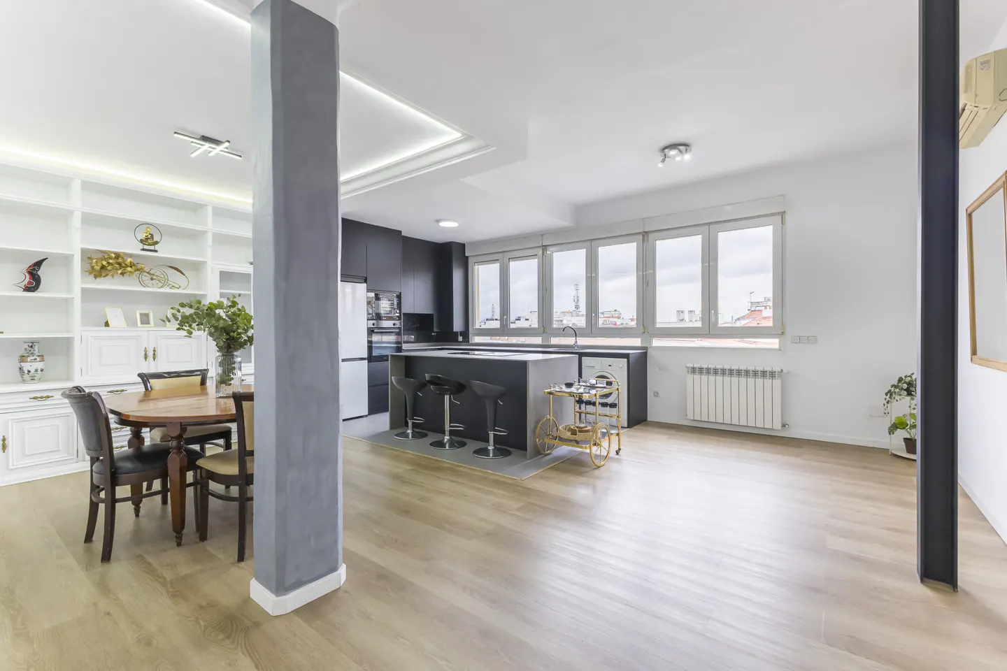 Open-concept apartment with wood floors, a black kitchen island with stools, and a dining area with a round table and white built-in shelves.