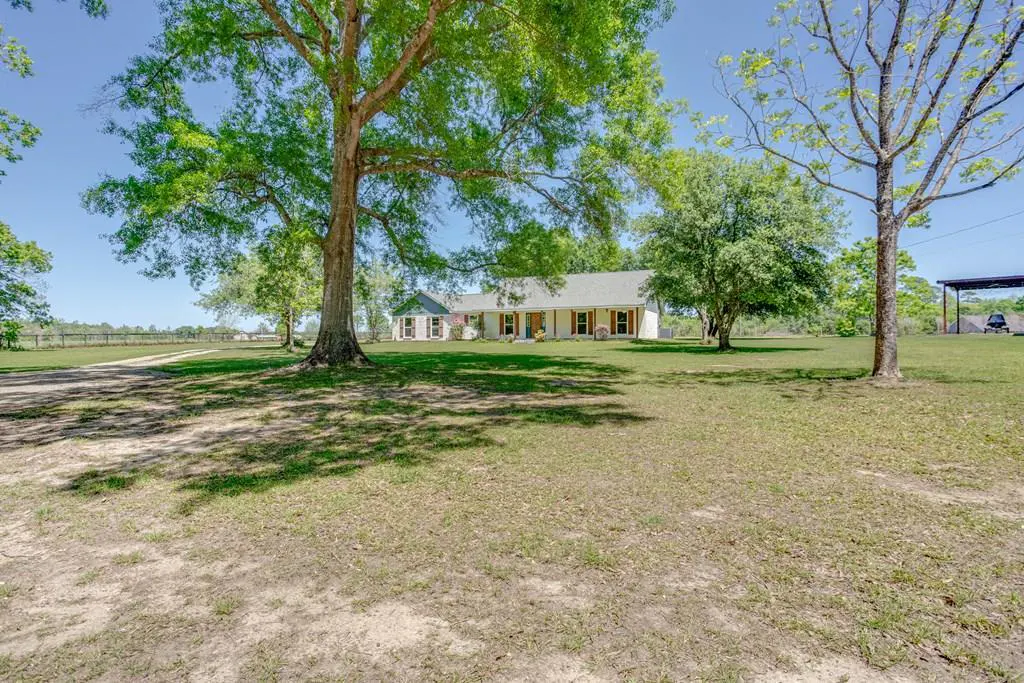 A ranch-style house with a large lawn and mature trees under a blue sky.
