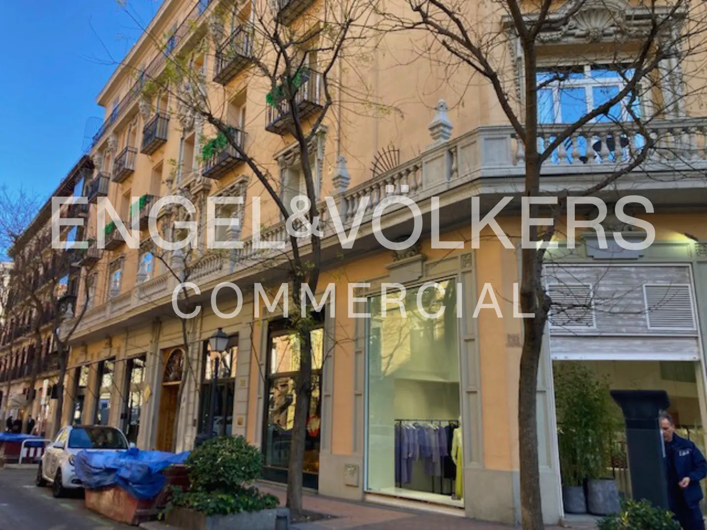 Engel & Völkers Commercial building with peach facade, ornate balconies, and street-level retail shops on a sunny day.