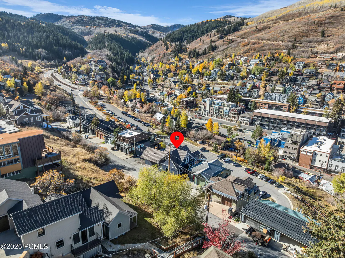 Aerial view of a blue house with a red pin on the roof, nestled in a mountain town with fall foliage.