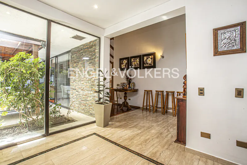 A bright foyer with marble floors, a small indoor garden, and wooden stools. Artwork hangs on the wall.
