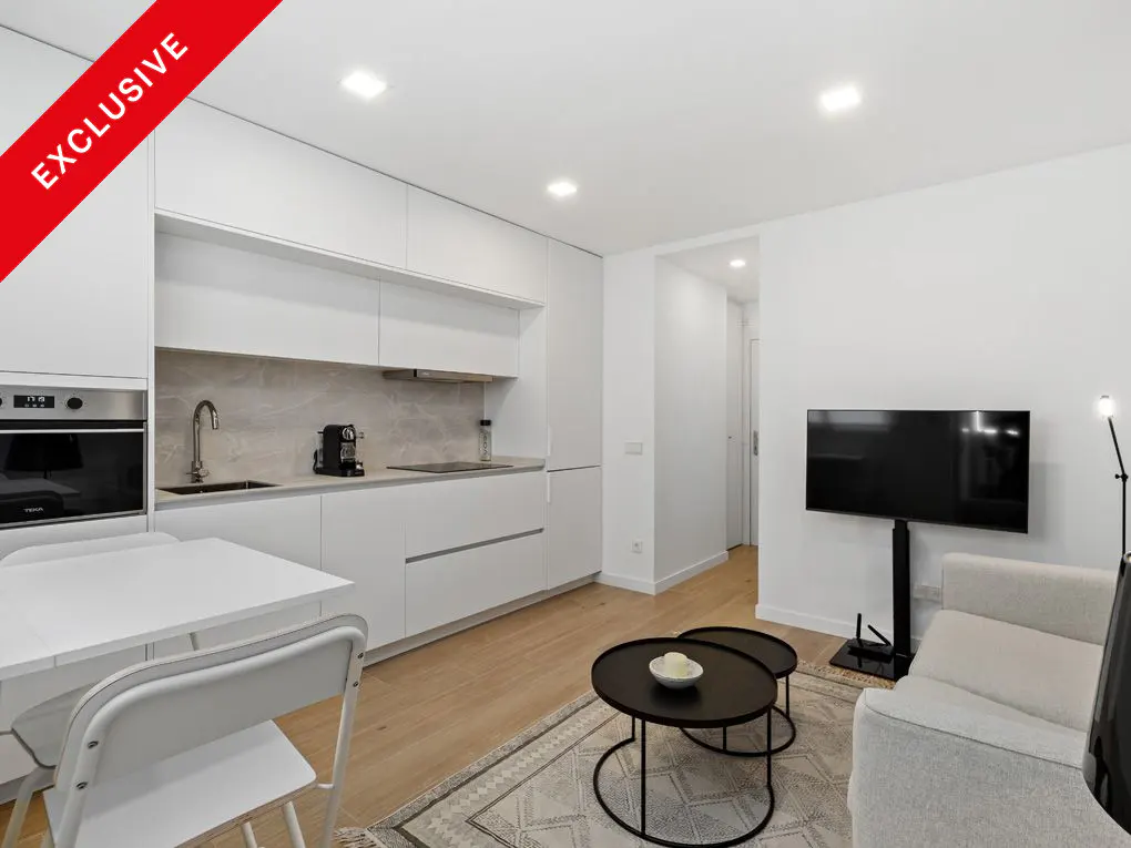 Bright, modern apartment interior with white kitchen cabinets, table, and living area with black tables and TV. "Exclusive" banner.