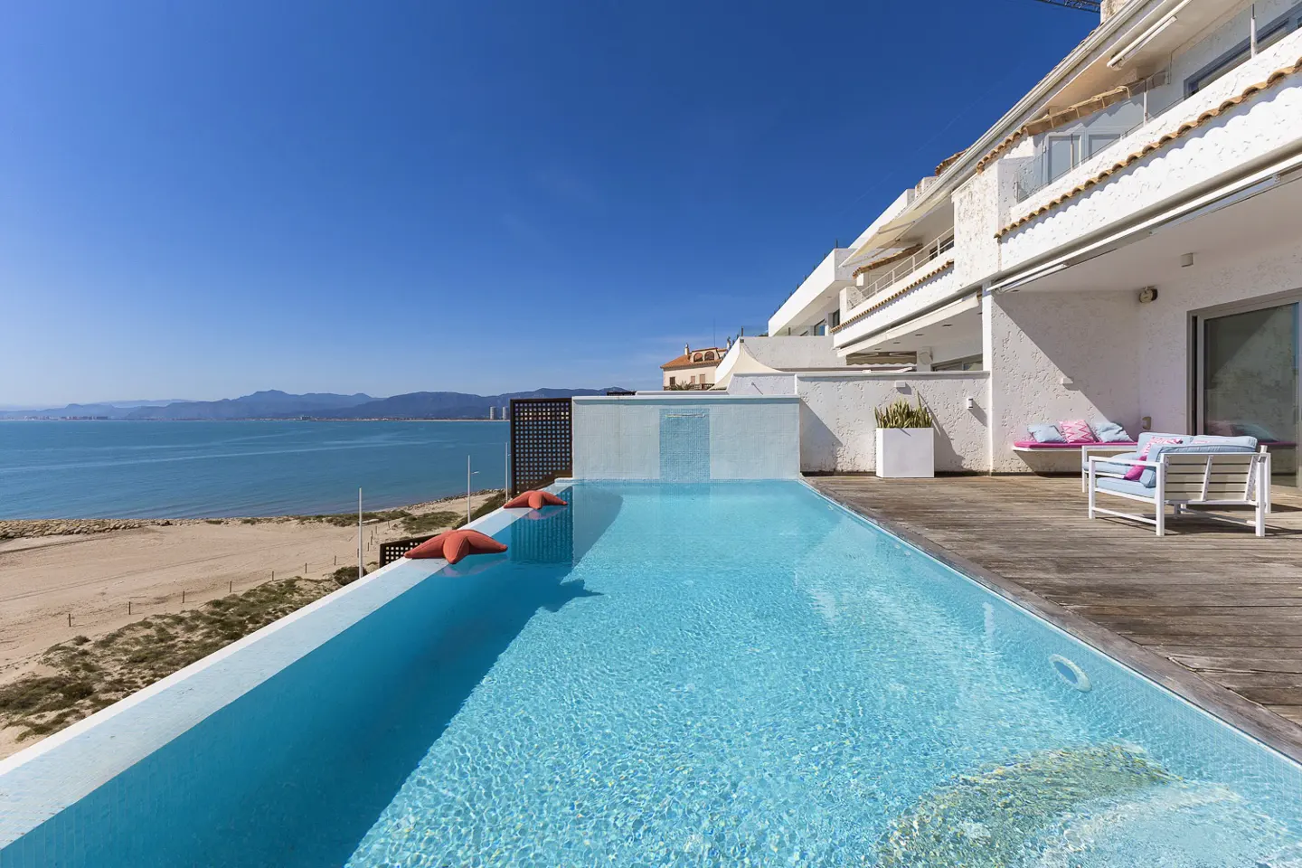 Rooftop pool with ocean view. Two orange starfish sit on the pool's edge. White building with patio furniture on the right.