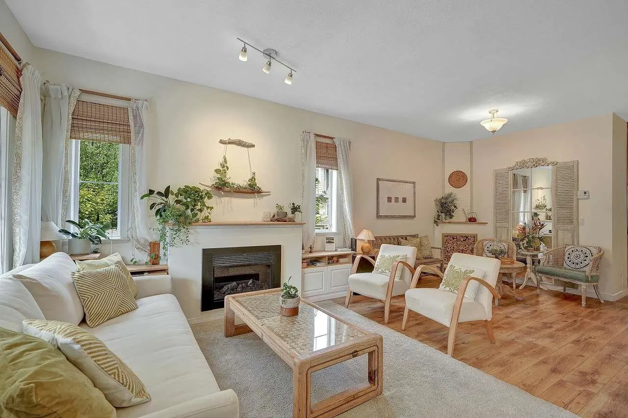A bright living room with a white sofa, fireplace, and two armchairs on a light gray rug and wood floor.