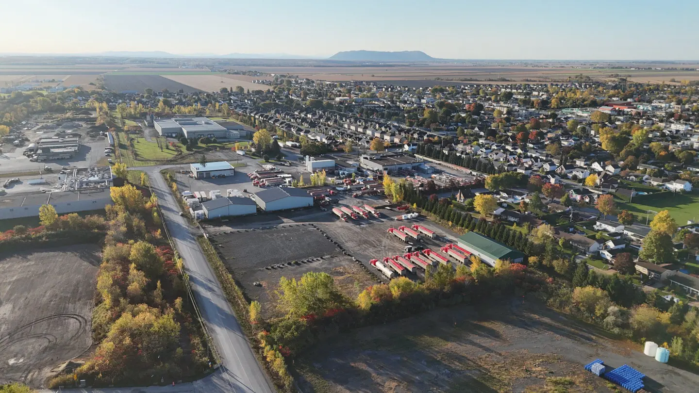 Aerial view of a rural town with industrial buildings, houses, and fields under a clear sky.