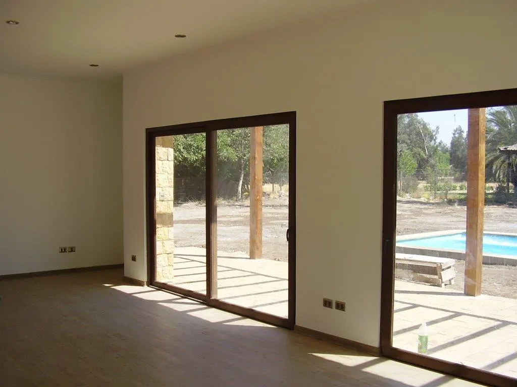 An interior view of a room with hardwood floors and two sliding glass doors with dark frames. Outside is a pool and trees.