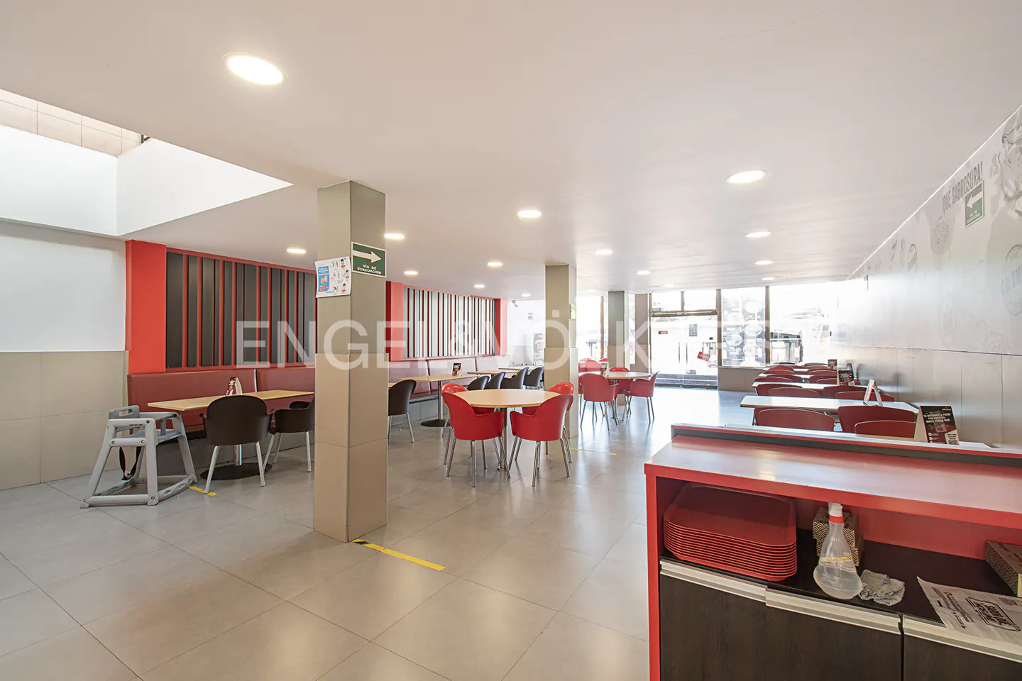 Bright, spacious restaurant interior with red chairs and booth seating. Gray tile floor and large windows.