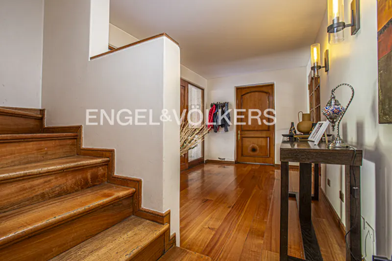 Interior view of a home's entryway with wooden stairs, hardwood floors, and a console table with a lamp.