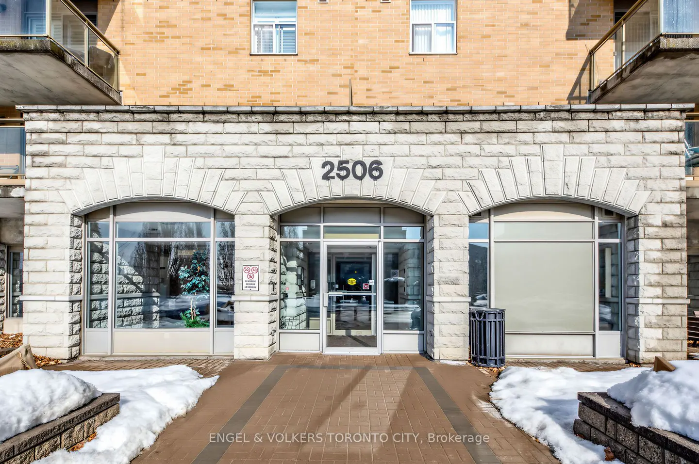 Building entrance with stone arches and glass doors. The address "2506" is above the door. Snow is on the ground.