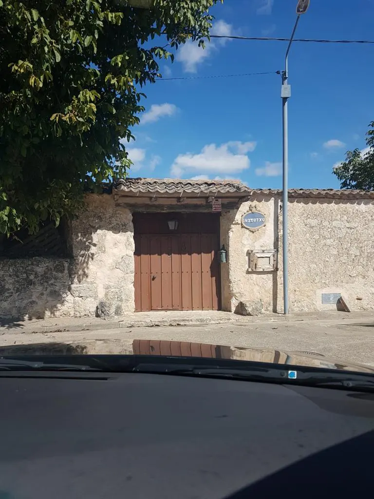 A brown wooden gate set into a rustic stone wall under a bright blue sky, viewed from inside a car.
