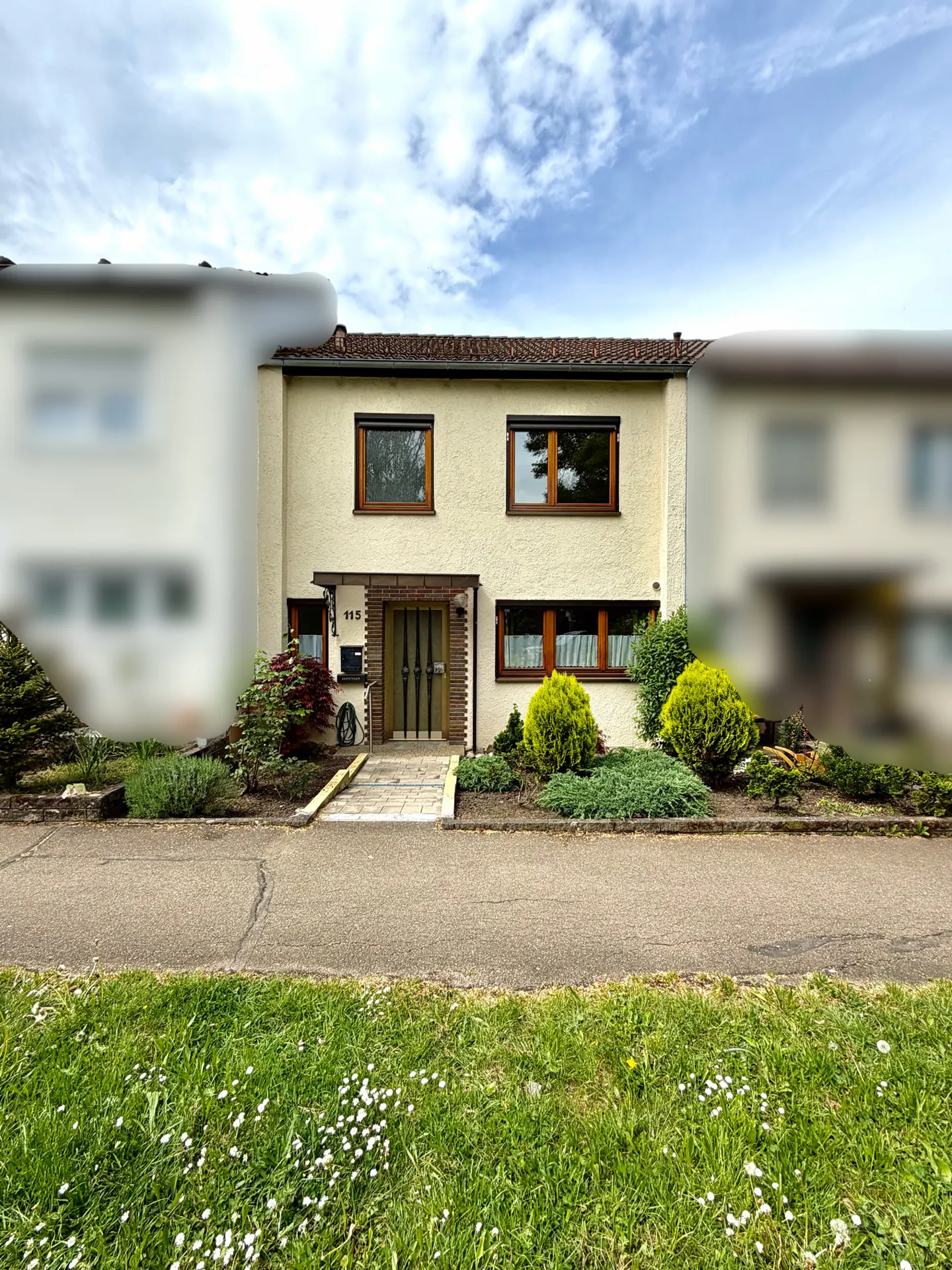 Two-story beige house with brown window frames and a stone walkway, set against a cloudy sky.