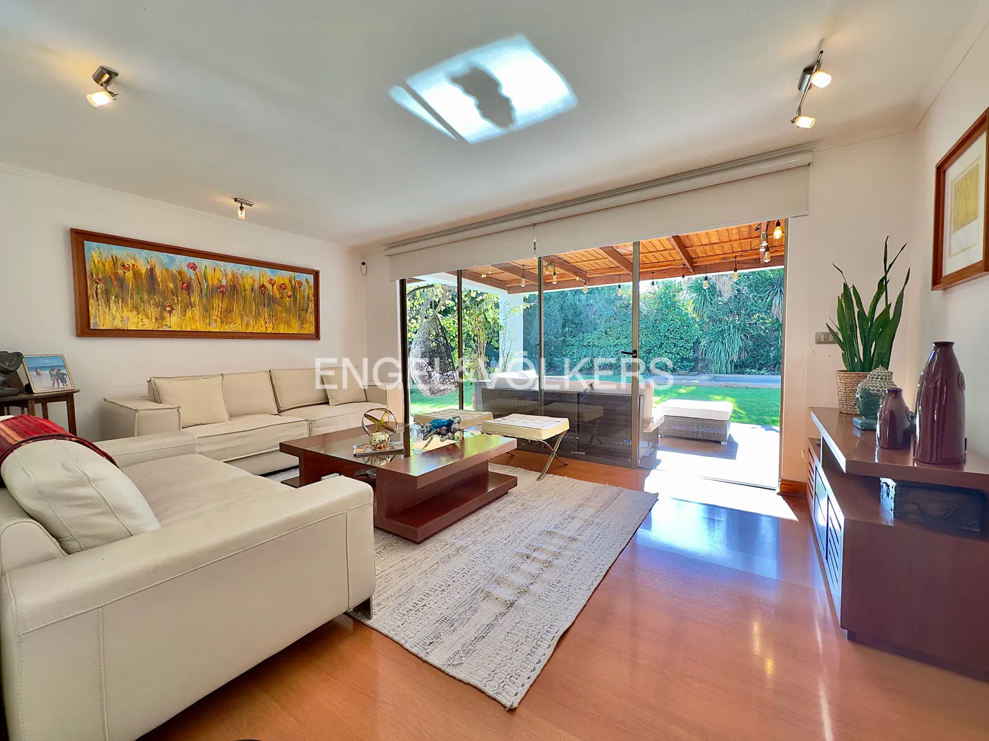 Bright living room with white sofas, a dark wood coffee table on a patterned rug, and a large glass door to a green backyard.