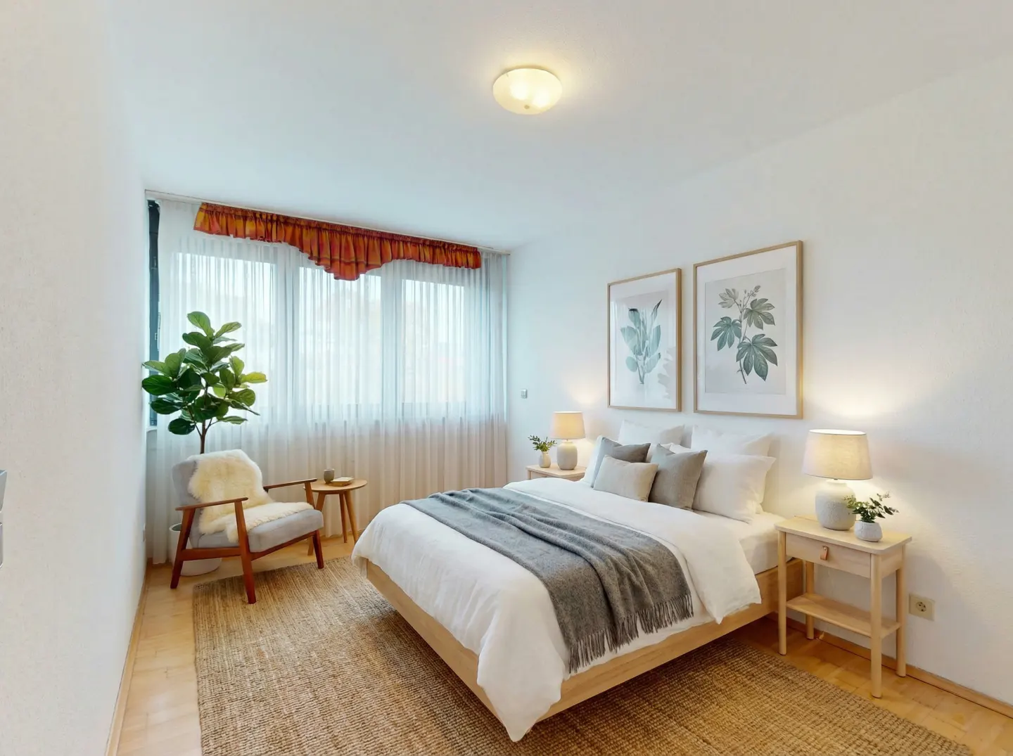 Bright bedroom with white walls, a wooden bed frame, and a gray throw blanket. Two botanical prints hang above the bed. A fiddle-leaf fig sits near a window.