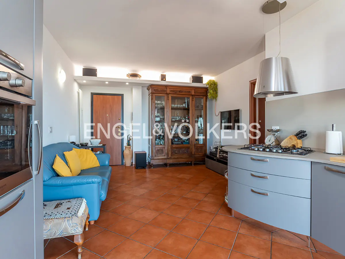 Open-concept living space with blue sofa, yellow pillows, and gray kitchen cabinets on terracotta tile floor.
