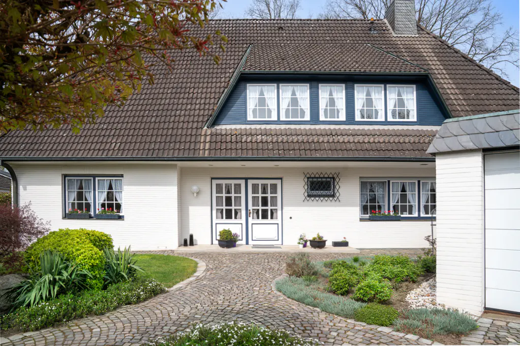 Two-story white house with a brown tile roof, blue trim, and a stone walkway leading to the front door.
