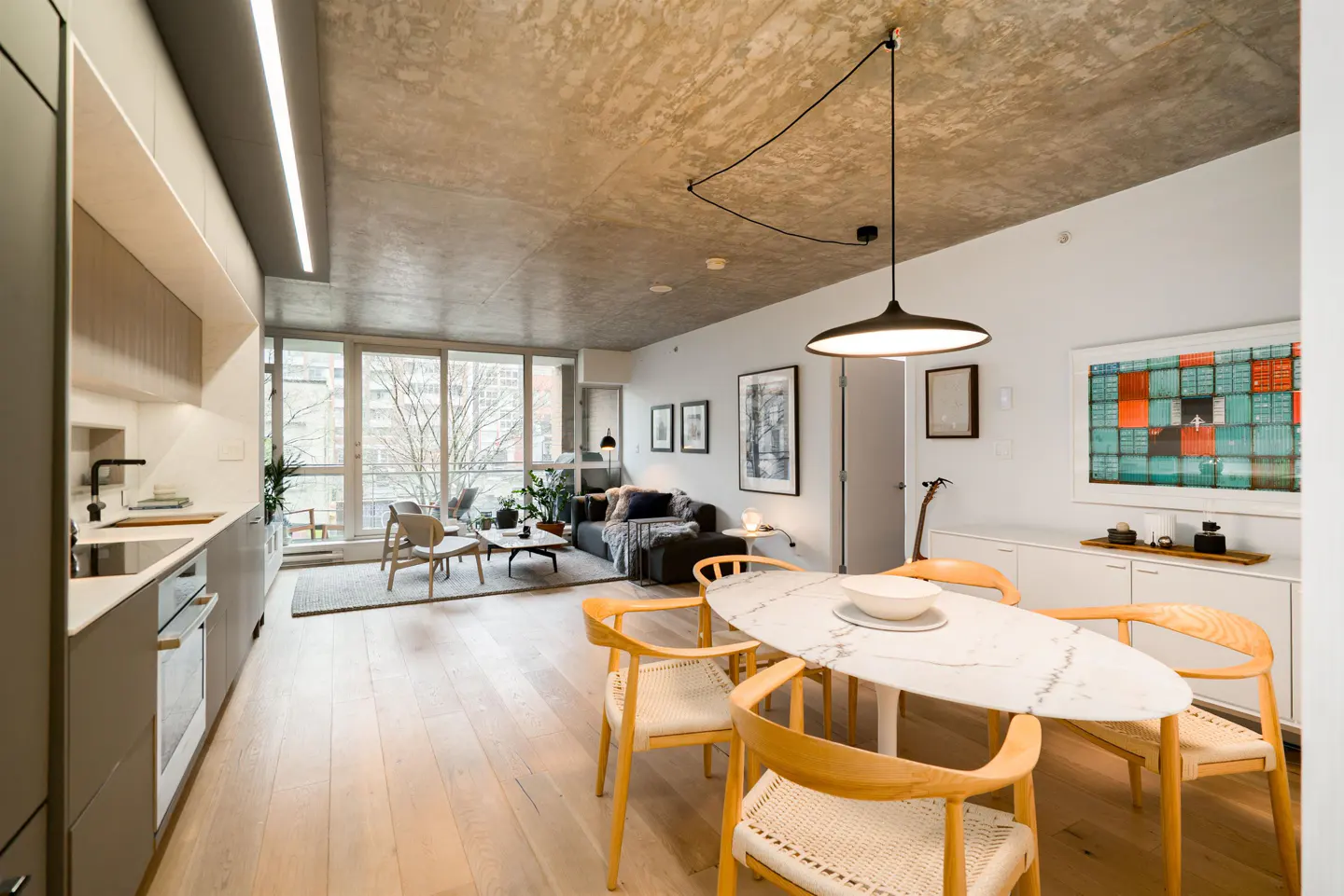Open-concept apartment with kitchen, dining, and living areas. Features a concrete ceiling, wood floors, and large windows.