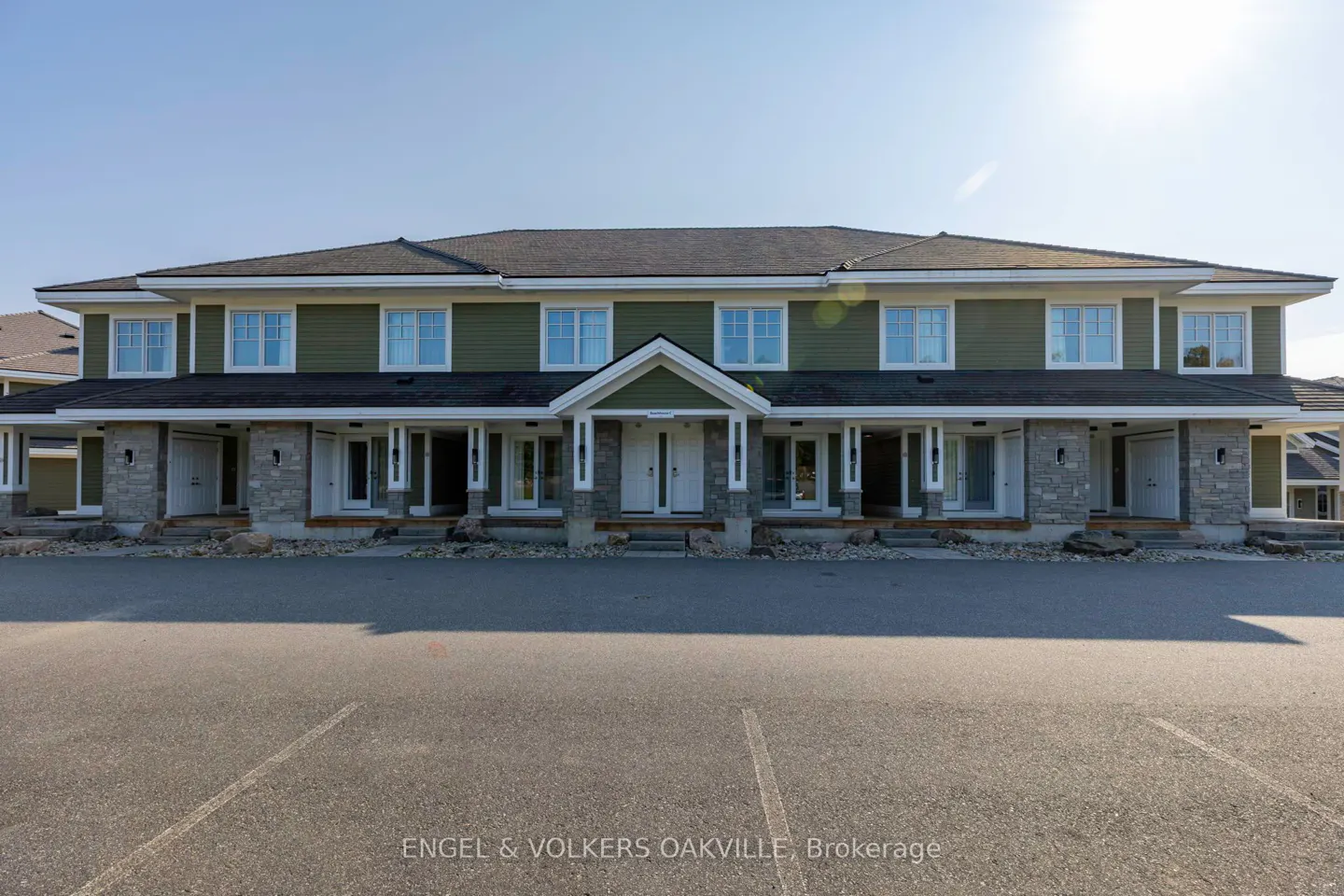 Two-story townhouse with green siding, white trim, and stone accents. Parking lot in front.