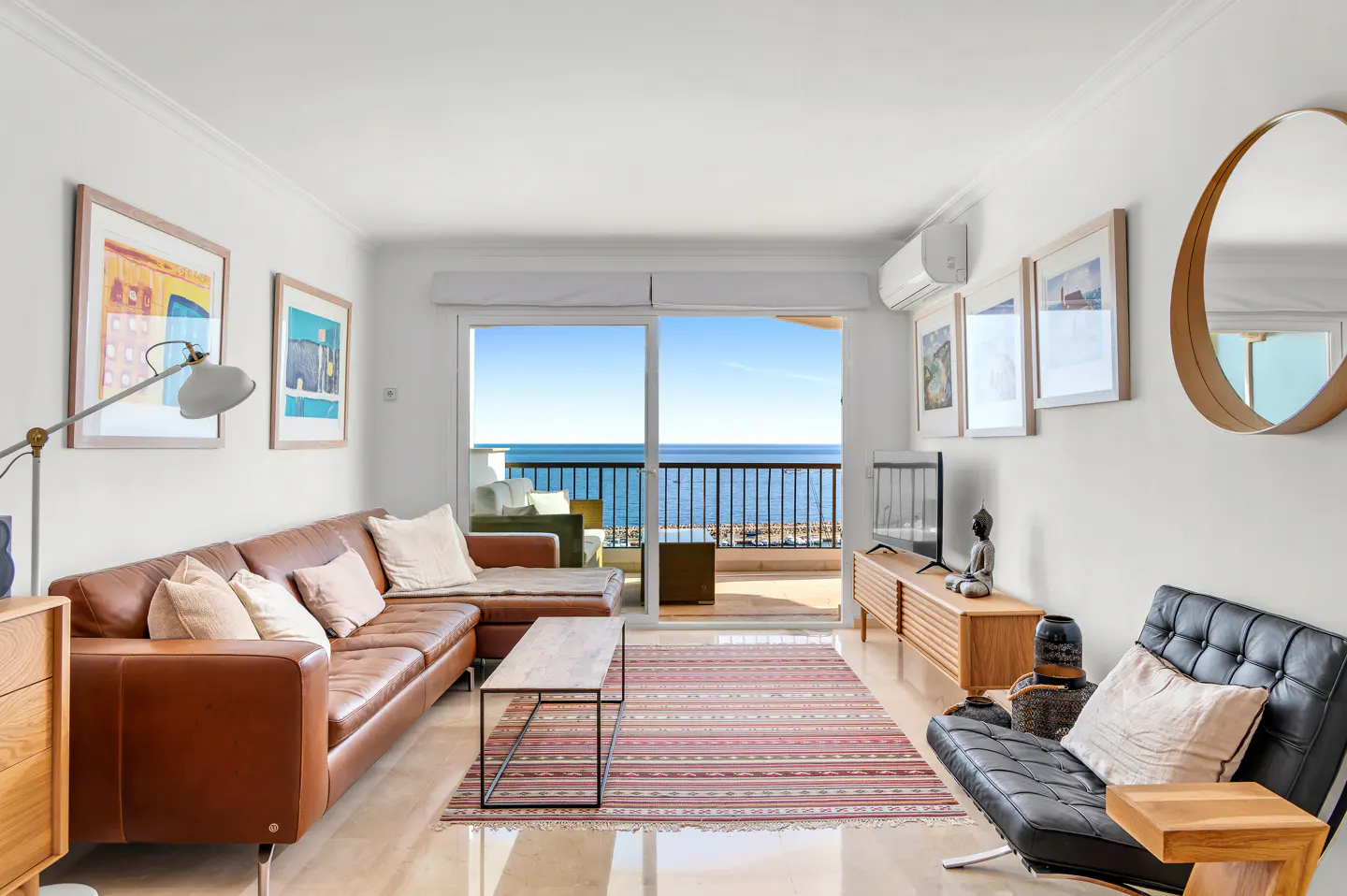 Bright living room with brown leather sofa, black chair, and ocean view through sliding glass doors.