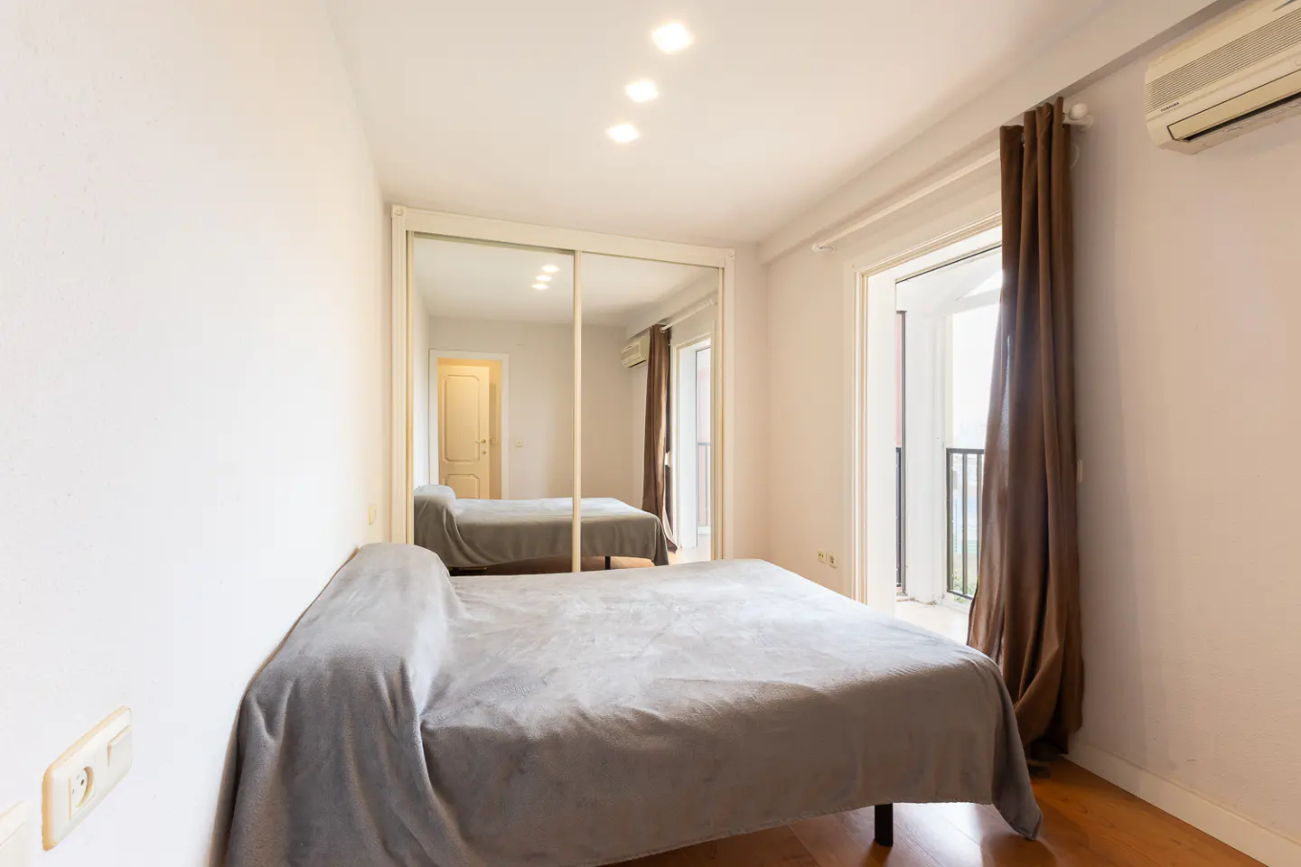 Bedroom with a bed covered in gray, a mirrored closet, and a balcony with brown curtains.
