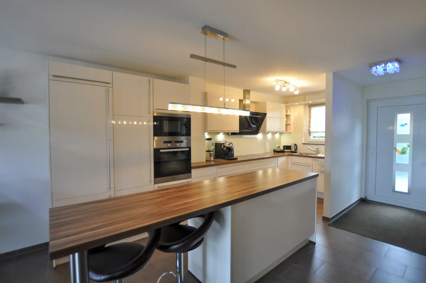 Modern kitchen with white cabinets, a wooden breakfast bar, two black stools, and stainless steel appliances.