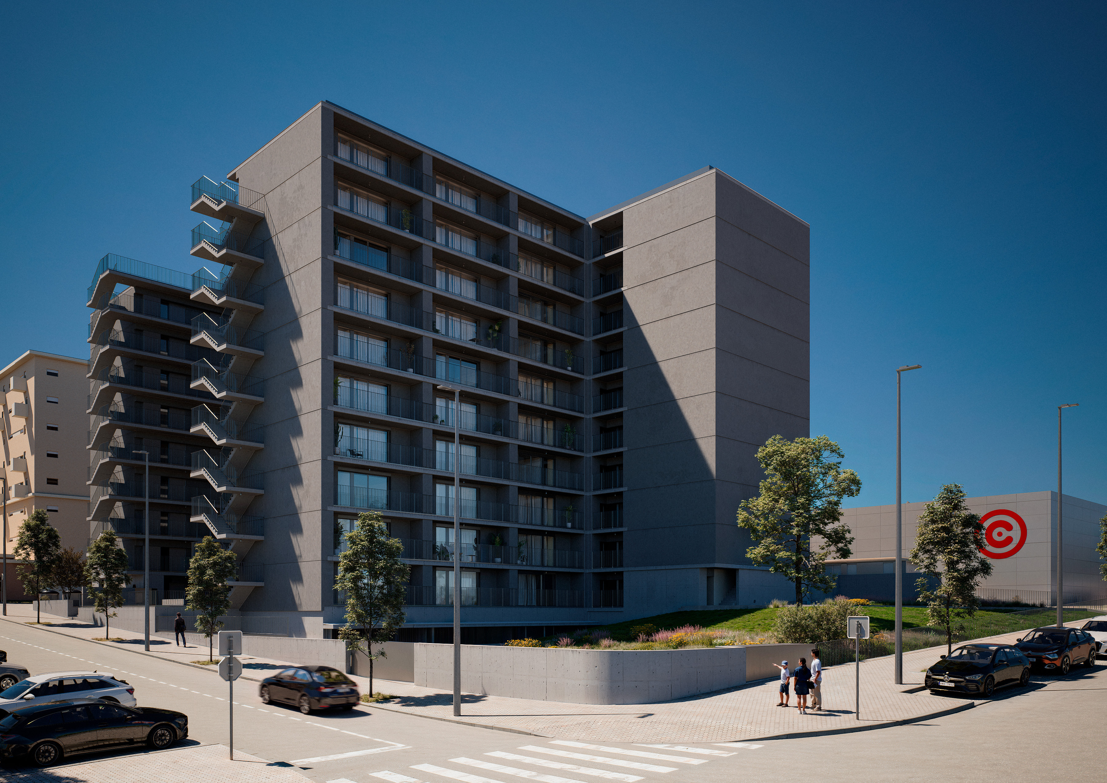 A modern grey apartment building with external staircases, street-level parking, and pedestrians on a sunny day.