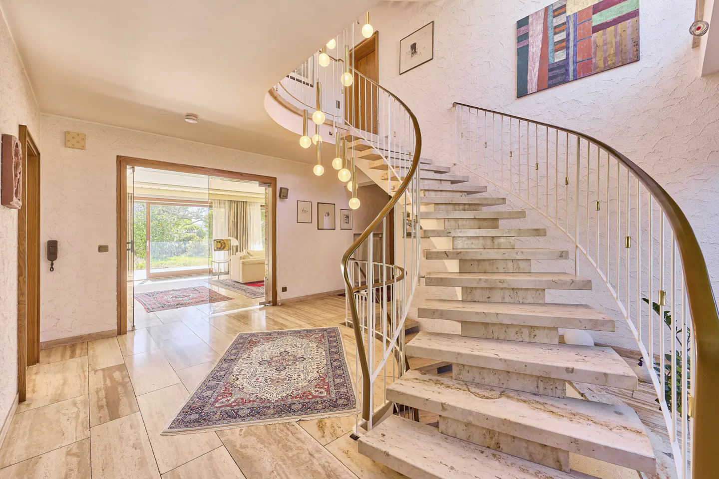 Bright foyer with marble floors, a spiral staircase with white railings, and a glass door leading to a sunlit living room.
