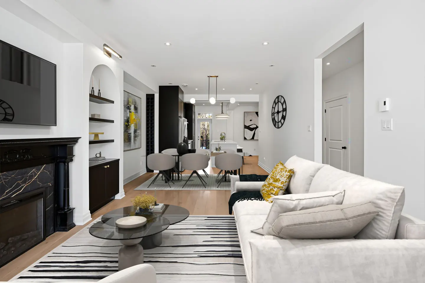 Bright, open-concept living room with white walls, a black fireplace, and a dining area visible in the background. A white sofa sits on a striped rug.