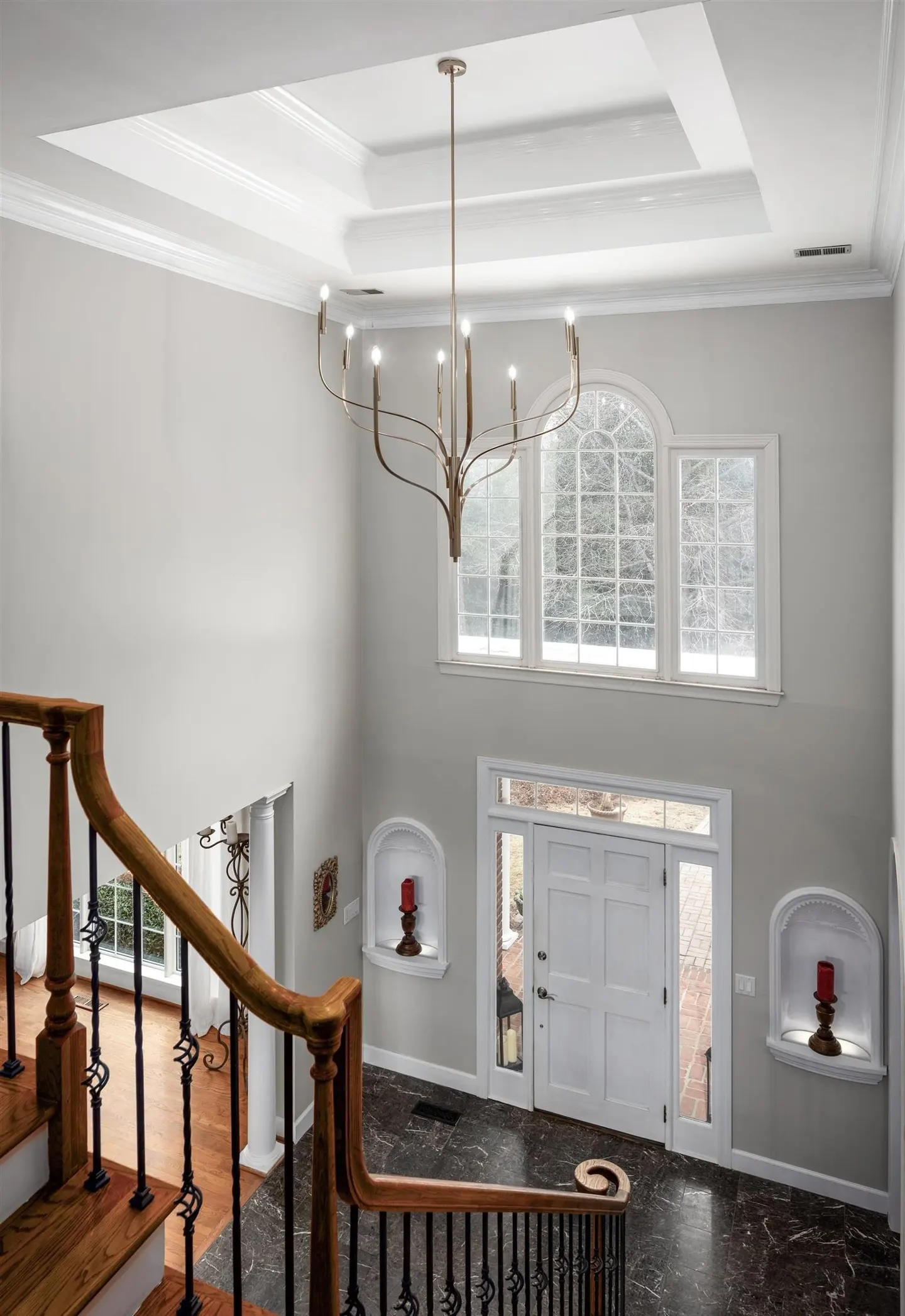 A high angle shot of a home's foyer with a staircase, chandelier, white walls, and a white front door.