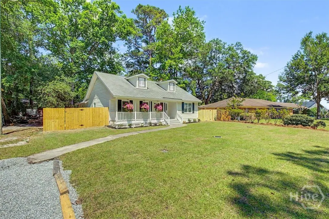 Exterior view of a white, one-story house with a green roof, a white porch with pink flowers, and a large green lawn.